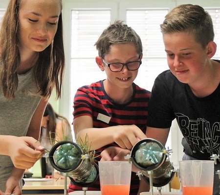 Drei Kinder arbeiten an einem Experiment zur Bodenversickerung in einem Klassenraum.