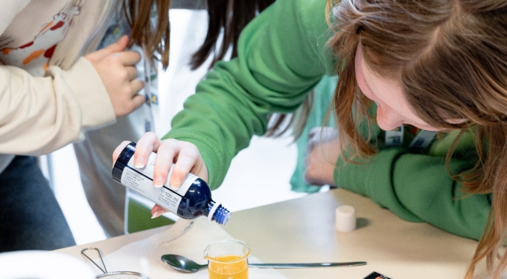 zwei Mädchen füllen konzentriert eine Flüssigkeit in einen kleinen Messbecher