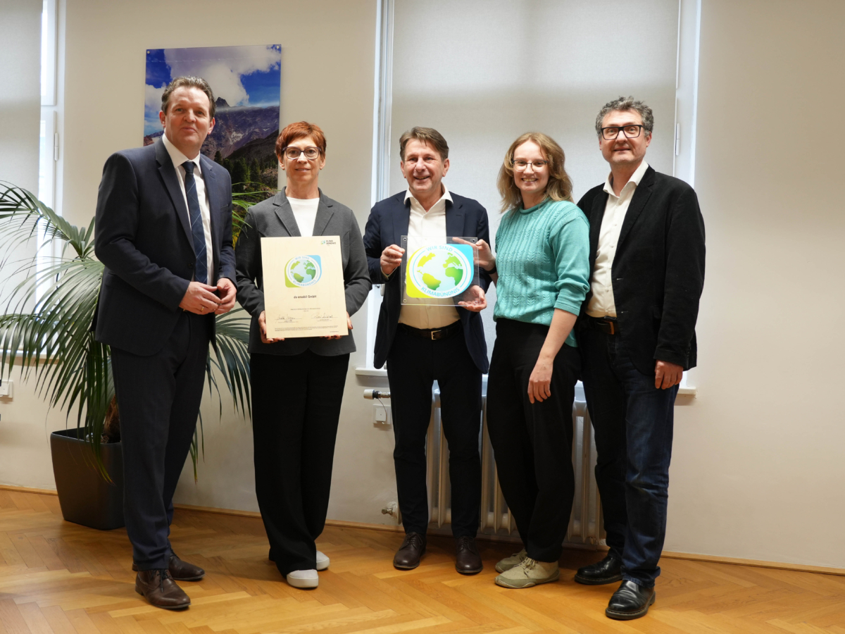 Fünf Personen präsentieren eine Urkunde und ein Klimabündnis-Schild in einem Raum