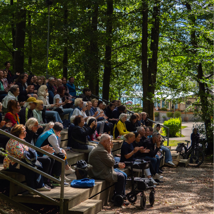 ältere Menschen sitzen zwischen bäumen auf einer hölzernen Tribüne