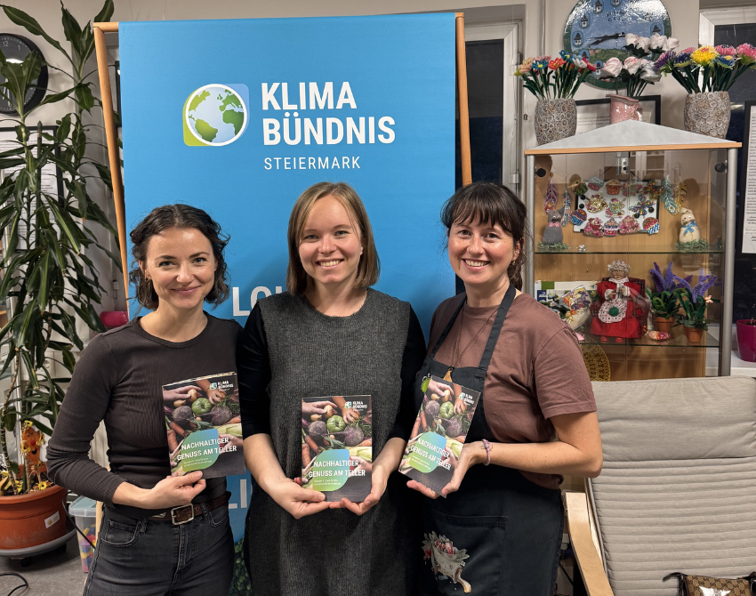 drei Frauen vor Klimabündnis Steiermark Rollup mit Broschüre in der Hand