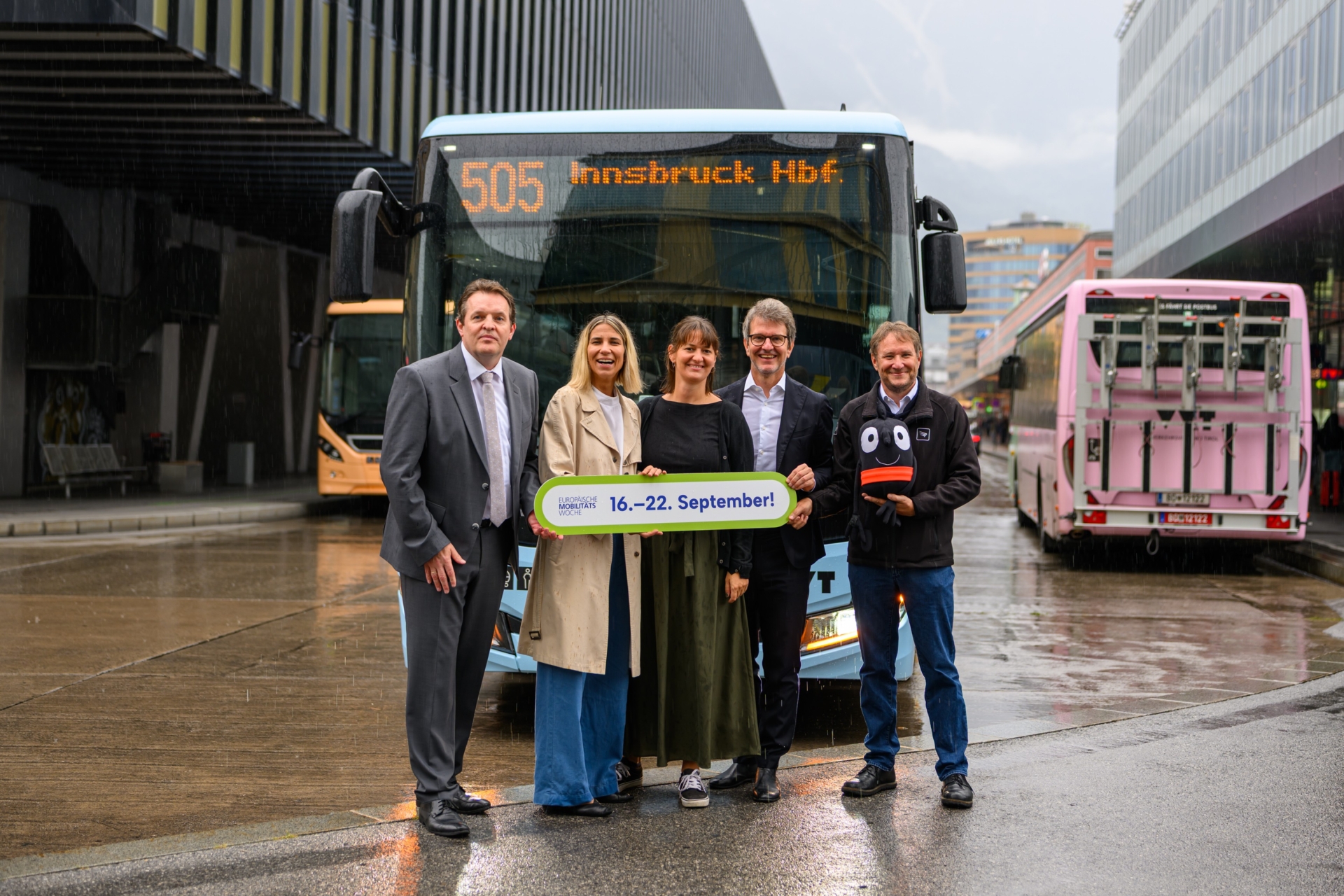 5 Menschen präsentieren das Logo der EMW vor einem Bus am Innsbrucker Hauptbahnhof